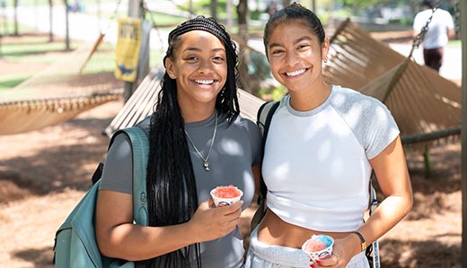 Two girls smile at the camera. They are both holding snowcones.